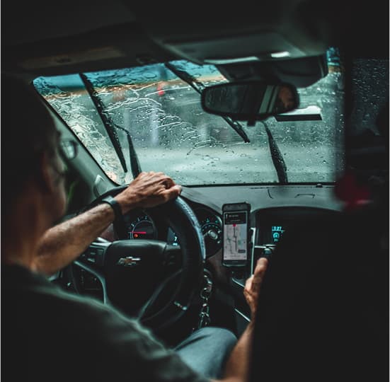 Homem ao volante verificando seu destino no GPS do celular acoplado ao suporte.